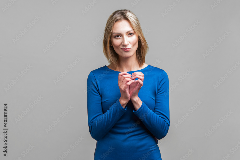 Portrait of cunning beautiful businesswoman in blue dress clasping hands and planning evil tricky prank or scheming, cheating with sly smile. indoor studio shot isolated on gray background Portrait of cunning beautiful businesswoman in blue dress clasping hands and planning evil tricky prank or scheming, cheating with sly smile. indoor studio shot isolated on gray background