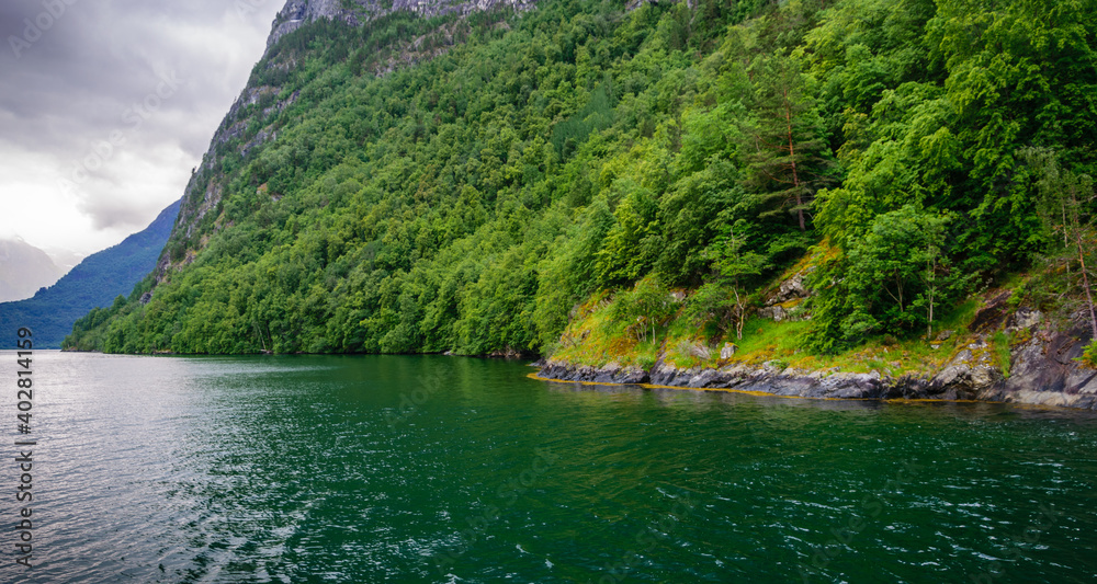 A fjord landscape with emerald water and steep cliffs covered with bright green vegetation.