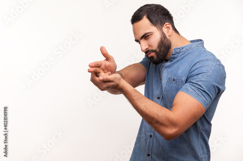 Assertive dangerous man with beard pointing fingers at target imitating weapon making shot, terrorism. Indoor studio shot isolated on white background
