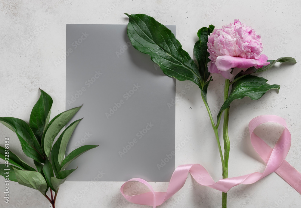 Fototapeta premium single delicate pink peony, pink ribbon and silver blank paper on a white background. Flower card. top view, place for text