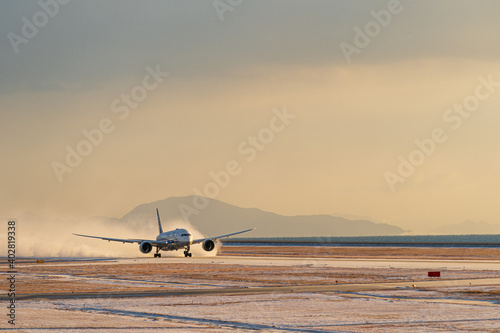 小雪舞う空港を雪煙を上げながら離陸する航空機