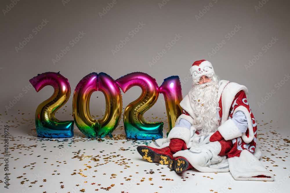 Santa sitting on the floor with colourful balloons in 2021 shape, photography for xmas and new year advertising. High quality photo