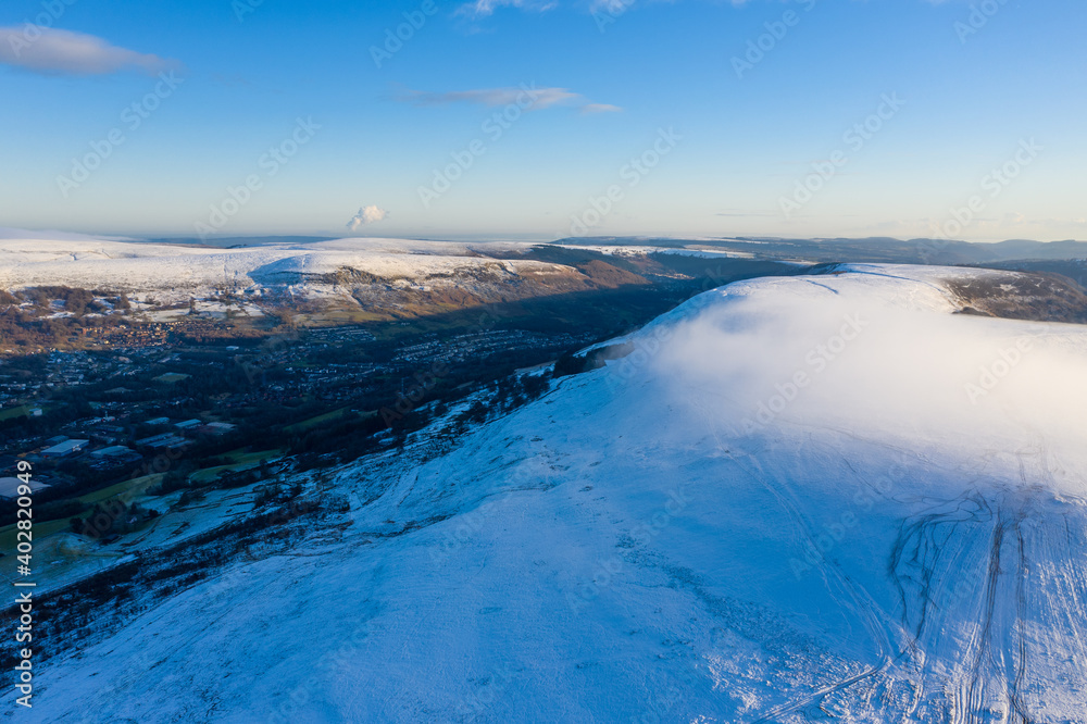 Aerial drone view of snow covered mountains and towns rising above the south east valleys, Wales
