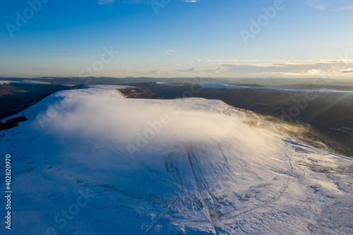 Aerial drone view of snow covered mountains and towns rising above the south east valleys, Wales