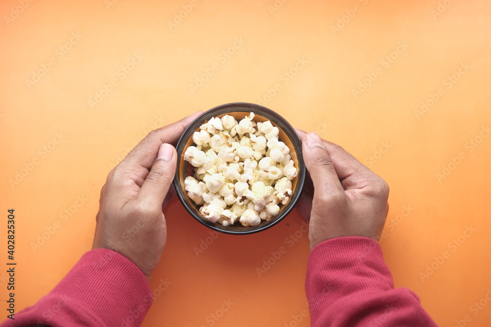  man's hand holding a bowl of popcorn on orange background 