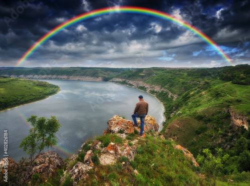 rainbow over the river. man on a cliff above the canyon