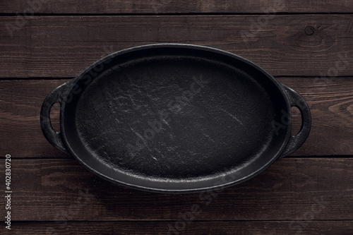 Empty cast iron plate for serving dishes on a wooden background, top view.