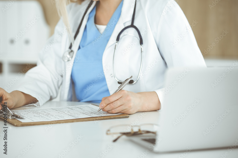 Unknown woman-doctor at work filling up medication history record form in clinic, close-up of clipboard