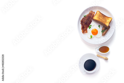 Breakfast, fresh butter toast, heart shaped fried eggs, smoked sausage and grilled bacon served with black coffee and honey on isolated white background, Top view.
