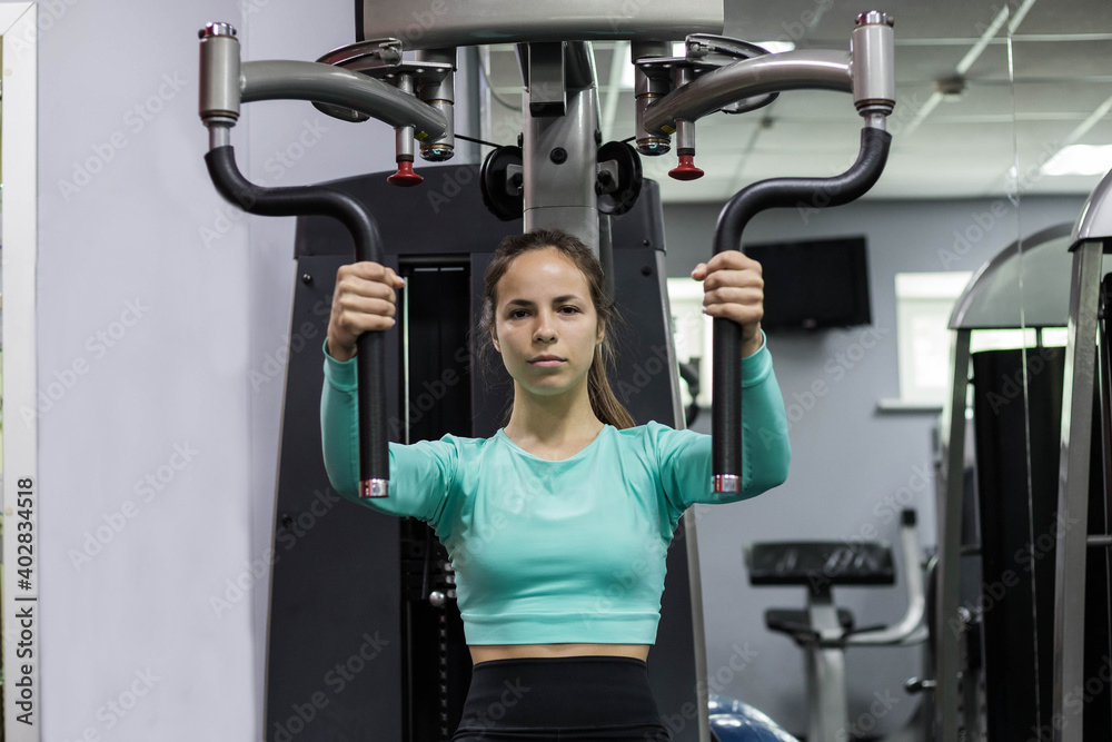 Woman doing fitness training on a butterfly machine with weights in gym or fitness club Woman doing fitness training on a butterfly machine with weights in gym or fitness club