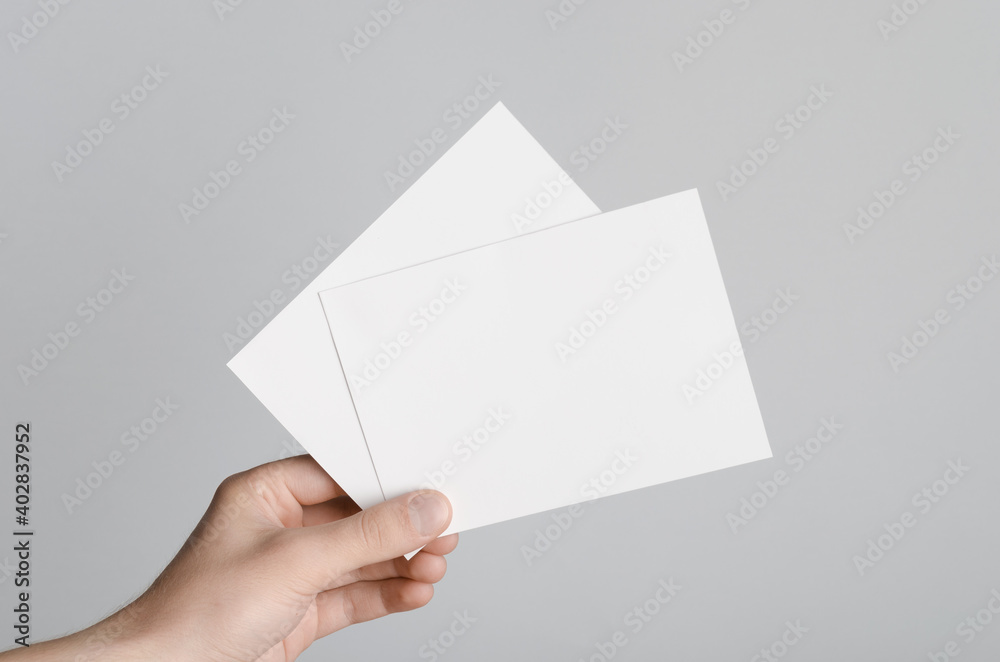 A6 Flyer / Postcard / Invitation Mock-Up - Male hands holding blank flyers on a gray background. A6 Flyer / Postcard / Invitation Mock-Up - Male hands holding blank flyers on a gray background.