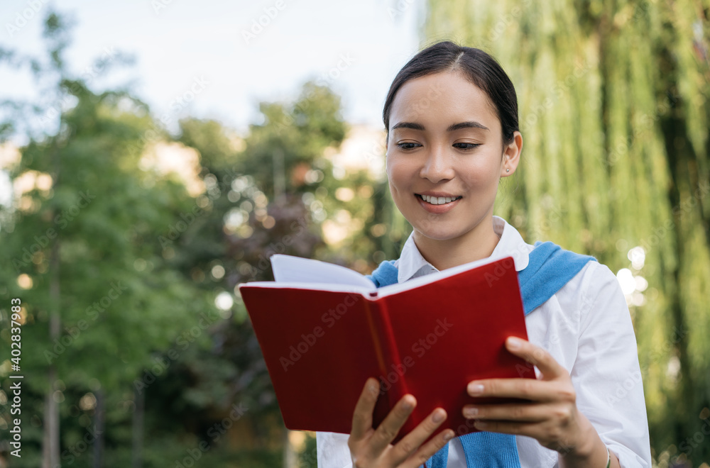 Close up portrait of beautiful asian woman reading book. Smiling student studying, learning language, sitting in park, education concept Close up portrait of beautiful asian woman reading book. Smiling student studying, learning language, sitting in park, education concept