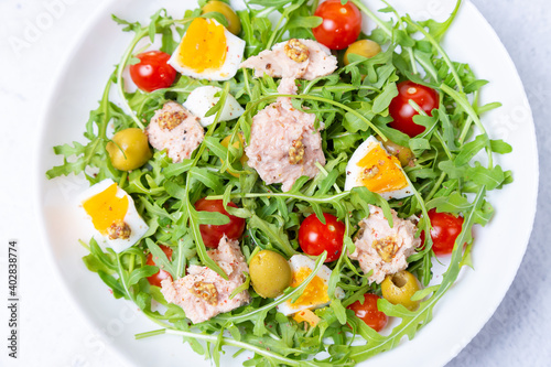 Salad with tuna, arugula, tomatoes, olives and eggs in a white plate. A traditional dish. Close-up.