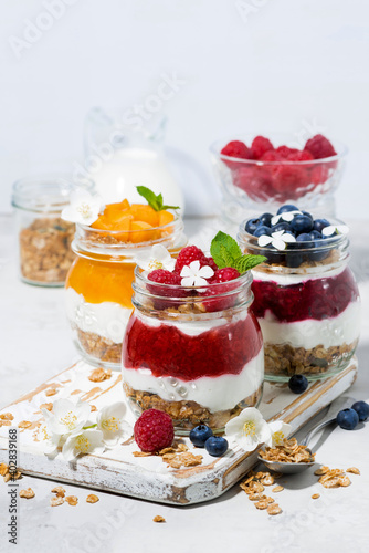 desserts with muesli, berry and fruit puree in jars on white background, vertical