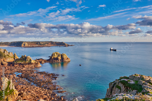 Image from the cliff path between La Corbiere and St Brelade's bay with calm sea and blue sky with clouds aand a ship anchored in the bay. Jersey, Channel Islands