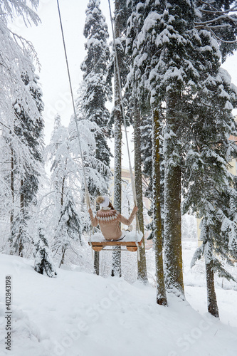 Young girl swinging on a long swing on snow forest mountain view.