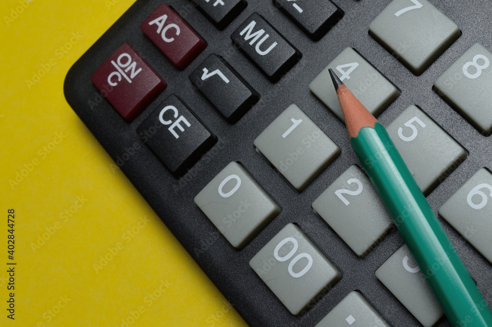 calculator and pencil lie on a yellow background. close-up.