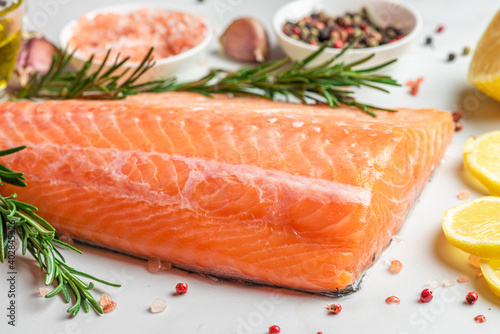 Fresh raw salmon fish fillet rich with omega 3 with cooking ingredients, herbs and lemon on white background