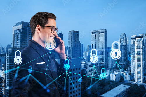 Fototapeta Naklejka Na Ścianę i Meble -  Eastern young handsome cybersecurity developer having conference call to protect clients confidential information by inventing solutions. IT lock icons over Bangkok city background.