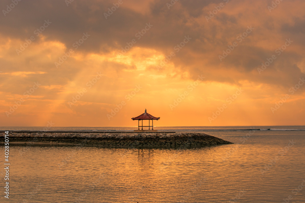 Beautiful sunrise on Bali in Sanur by the sea with a view over the beach to the sea. a temple and breakwater in the sea at sunrise. Hinuistic