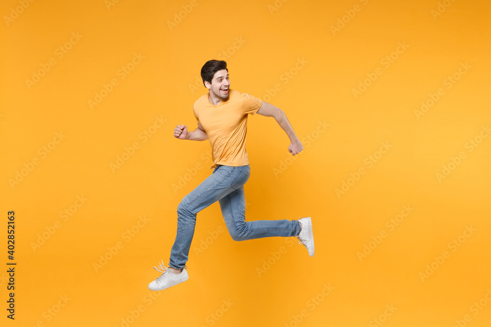 Full length side view of young caucasian fun happy energetic hurrying man 20s wearing casual basic t-shirt jeans high jumping up running look back isolated on yellow color background studio portrait. Full length side view of young caucasian fun happy energetic hurrying man 20s wearing casual basic t-shirt jeans high jumping up running look back isolated on yellow color background studio portrait.