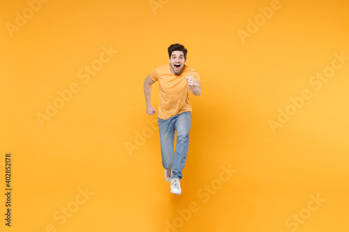 Full length young energetic active sporty healthy fast happy surprised man 20s wearing casual basic t-shirt jeans high jumping up running looking camera isolated on yellow background studio portrait.
