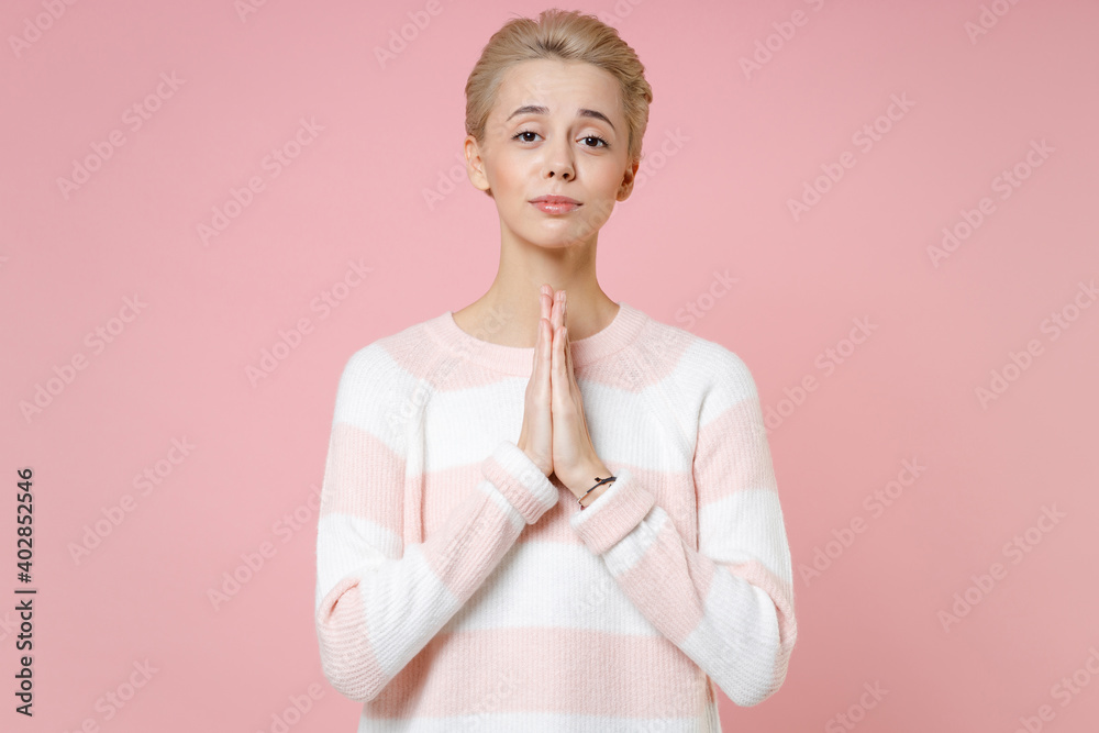 Young nice caucasian blonde woman 20s with short haircut nude makeup wearing casual knitted sweater hands folded in prayer looking camera isolated on pastel pink color background studio portrait. Young nice caucasian blonde woman 20s with short haircut nude makeup wearing casual knitted sweater hands folded in prayer looking camera isolated on pastel pink color background studio portrait.