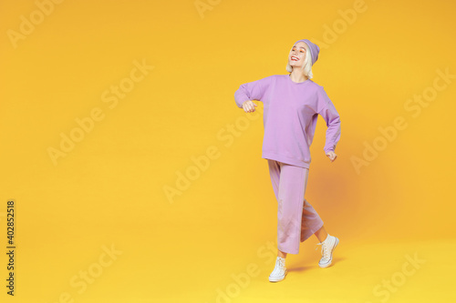 Full length of young fun blonde caucasian woman 20s bob haircut wearing casual basic purple suit beanie hat standing holding hands crossed folded isolated on yellow color background studio portrait.
