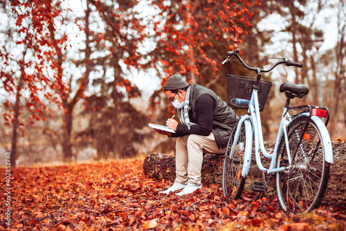 Aisian man with protective mask is sitting outside and writing next to this bike, in autumn time. photo