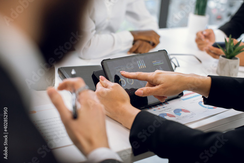 Cropped close up image of unrecognizable multiracial businesspeople having meeting at office. Focus on female hands touching digital tablet pc with business diagram infographics