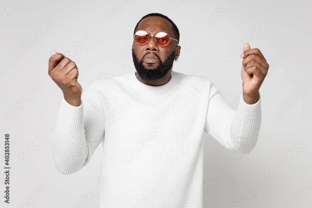 Naklejka premium Displeased upset crying young african american man 20s wearing basic sweater eyeglasses standing spreading hands clenching fists looking camera isolated on white color wall background studio portrait.