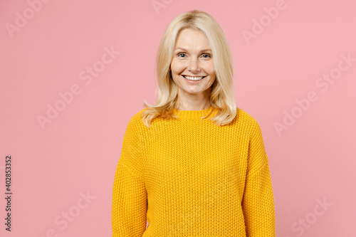 Smiling cheerful beautiful elderly gray-haired blonde woman lady 40s 50s years old wearing yellow casual sweater standing and looking camera isolated on pastel pink color background studio portrait. photo