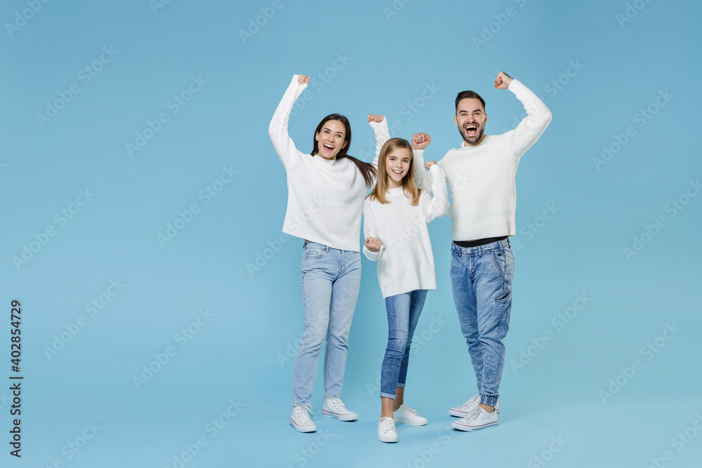 Full length of happy joyful young parents mom dad with child kid daughter teen girl in sweaters clenching fists like winner isolated on blue background studio portrait. Family day parenthood concept. Full length of happy joyful young parents mom dad with child kid daughter teen girl in sweaters clenching fists like winner isolated on blue background studio portrait. Family day parenthood concept.