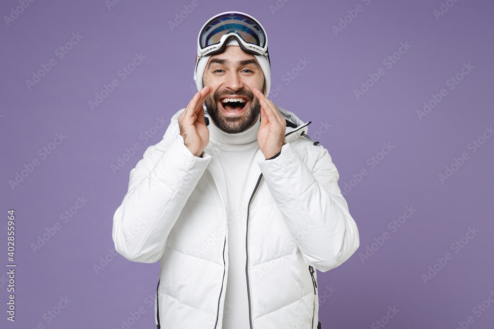 Funny skier man in white windbreaker jacket ski goggles mask scream news with hands near mouth spend extreme weekend winter in mountains isolated on purple background. People lifestyle hobby concept. Funny skier man in white windbreaker jacket ski goggles mask scream news with hands near mouth spend extreme weekend winter in mountains isolated on purple background. People lifestyle hobby concept.