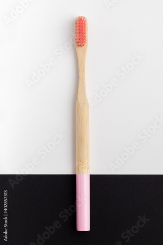 Bamboo toothbrush with pink bristles on a black and white background.