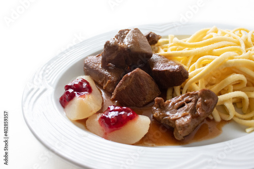 Wildragout, Wildschweingulasch mit Spätzle, Preiselbeeren und Birne auf weißem Hintergrund 