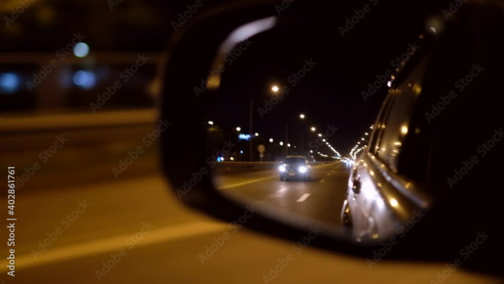 mirror of car driving on a night city road with a car following 