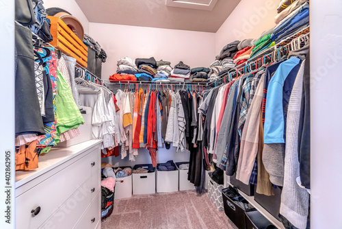 Clothes inside a walk in closet of home with carpet on floor and white wall