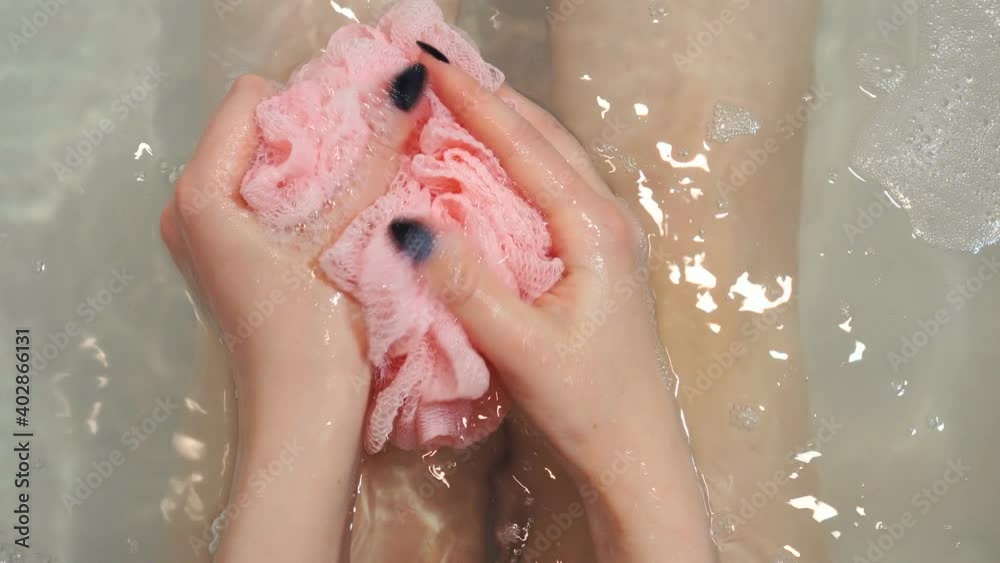Woman holding pink sponge and soaping it using shower gel.
