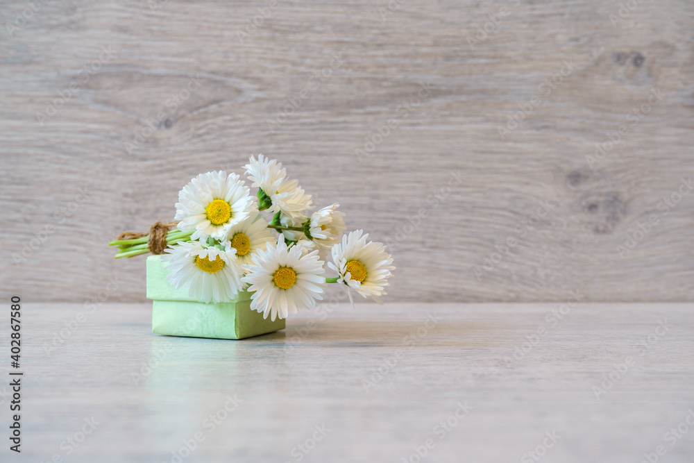Bouquet of fresh white Marguerite daisy flowers and small gift box lying on light background. Spring or summer beautiful still life. Greeting card for women's or mother's day. Holiday concept