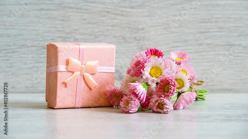 Bouquet of fresh pink Marguerite daisy flowers and small gift box lying on light background. Spring or summer beautiful still life. Greeting card for women's or mother's day. Holiday concept
