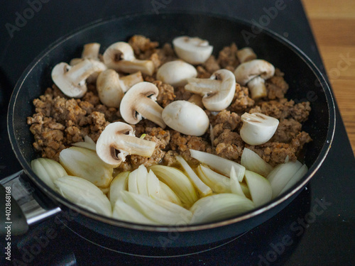 Pork minced meat in frying pan with onion, garlic and champignons 