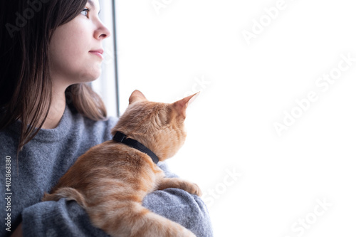 Pretty woman holding a cat and looking out the window
