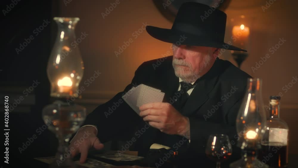 Lit by candlelight and oil lamps a gambler from the Victorian era plays a card game called Faro with someone off scene.