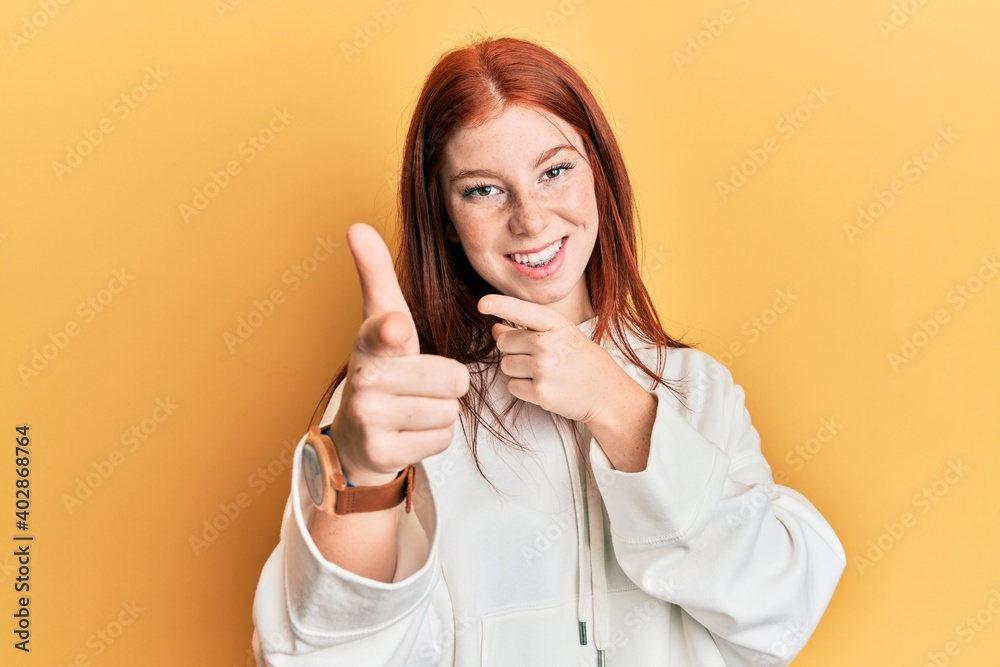 Young red head girl wearing casual sweatshirt pointing fingers to camera with happy and funny face. good energy and vibes. Young red head girl wearing casual sweatshirt pointing fingers to camera with happy and funny face. good energy and vibes.