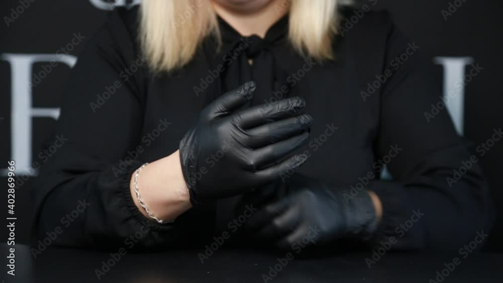Woman in a black shirt wears black gloves on her hands. Manicure master wearing black rubber gloves. Arms in a black rubber gloves. Blonde woman in a black shirt protecting her hands with a black rubb Woman in a black shirt wears black gloves on her hands. Manicure master wearing black rubber gloves. Arms in a black rubber gloves. Blonde woman in a black shirt protecting her hands with a black rubb