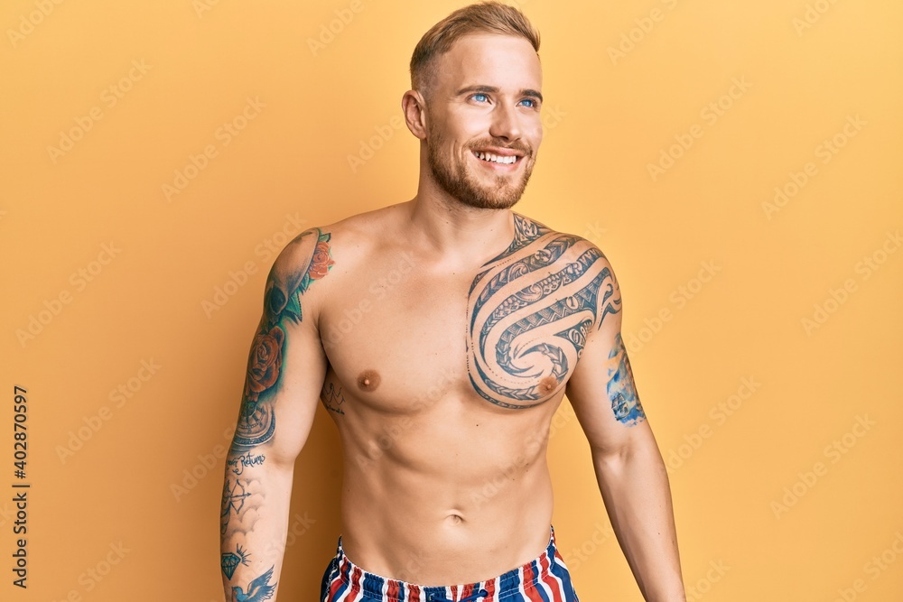 Fototapeta premium Young caucasian man wearing swimwear shirtless looking away to side with smile on face, natural expression. laughing confident.