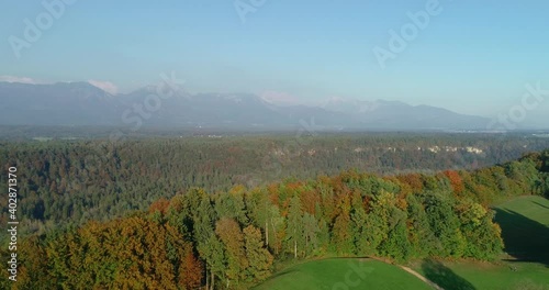 Drone aerial view of meadow grassland and forest. Beautiful sunset colors in autumn. Ljubljana basin and Alps mountains in the distance in Slovenia. Backward moving photo
