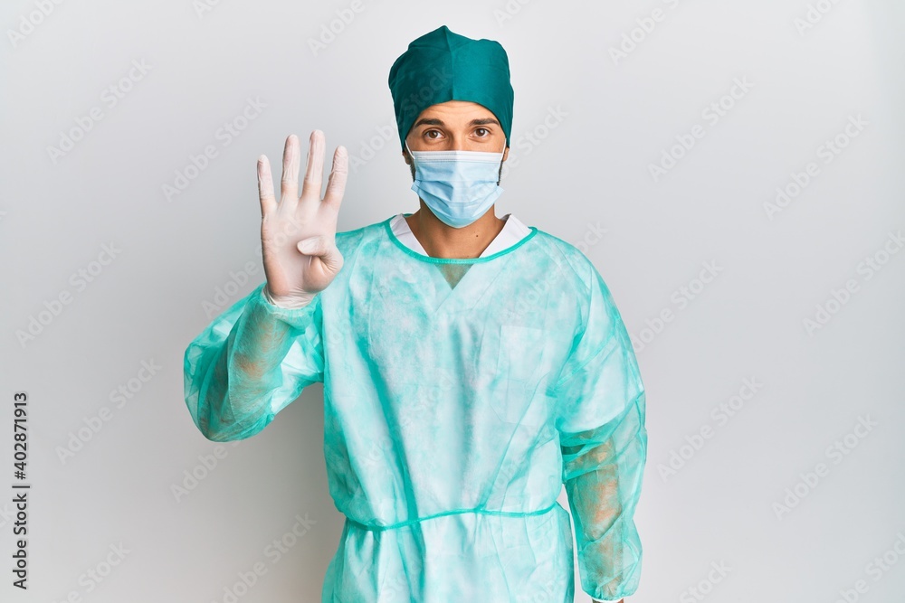 Young handsome man wearing surgeon uniform and medical mask showing and pointing up with fingers number four while smiling confident and happy. Young handsome man wearing surgeon uniform and medical mask showing and pointing up with fingers number four while smiling confident and happy.