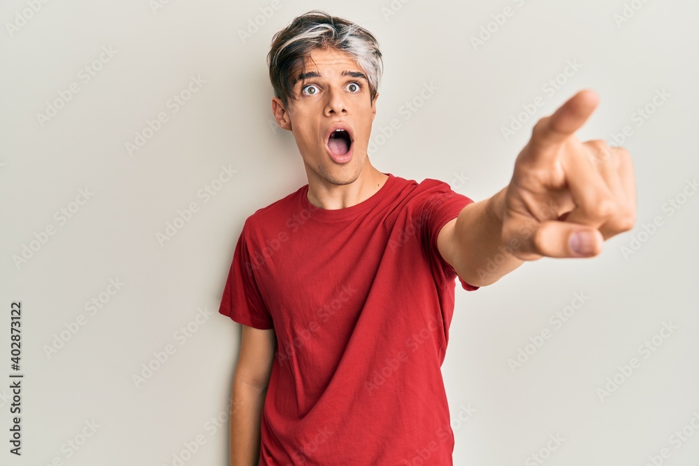 Young hispanic man wearing casual clothes pointing with finger surprised ahead, open mouth amazed expression, something on the front Young hispanic man wearing casual clothes pointing with finger surprised ahead, open mouth amazed expression, something on the front